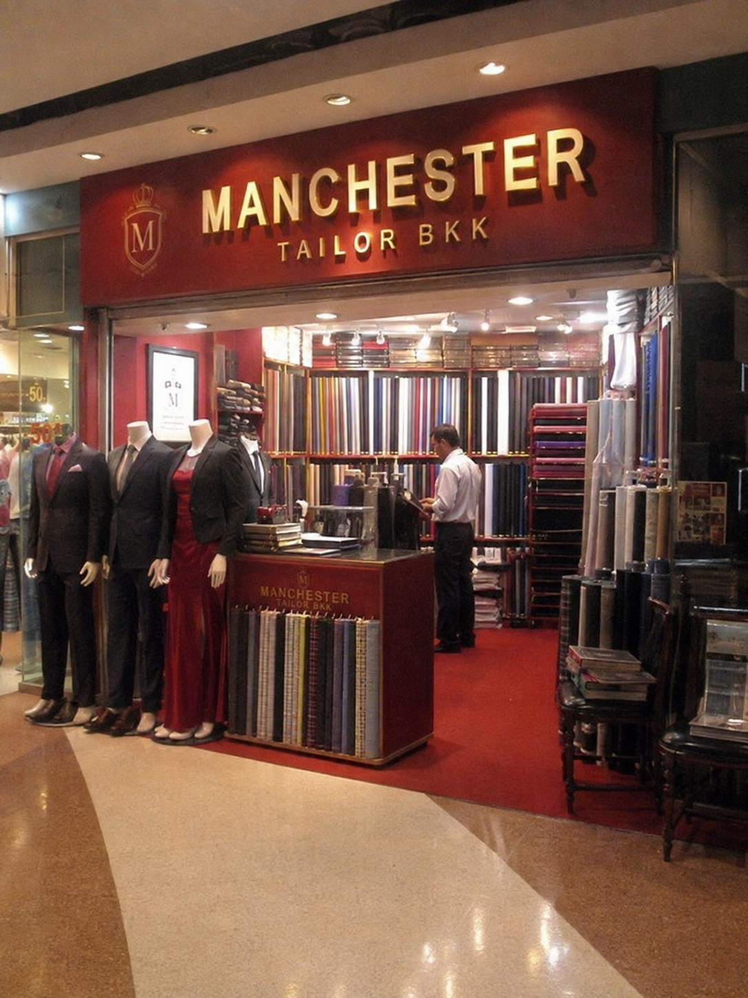 The Manchester Tailor BKK storefront in Bangkok with fabric rolls and suited mannequins